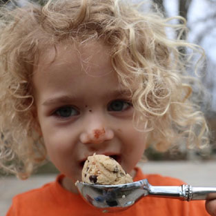 Boy with long curly hair eating cookie dough